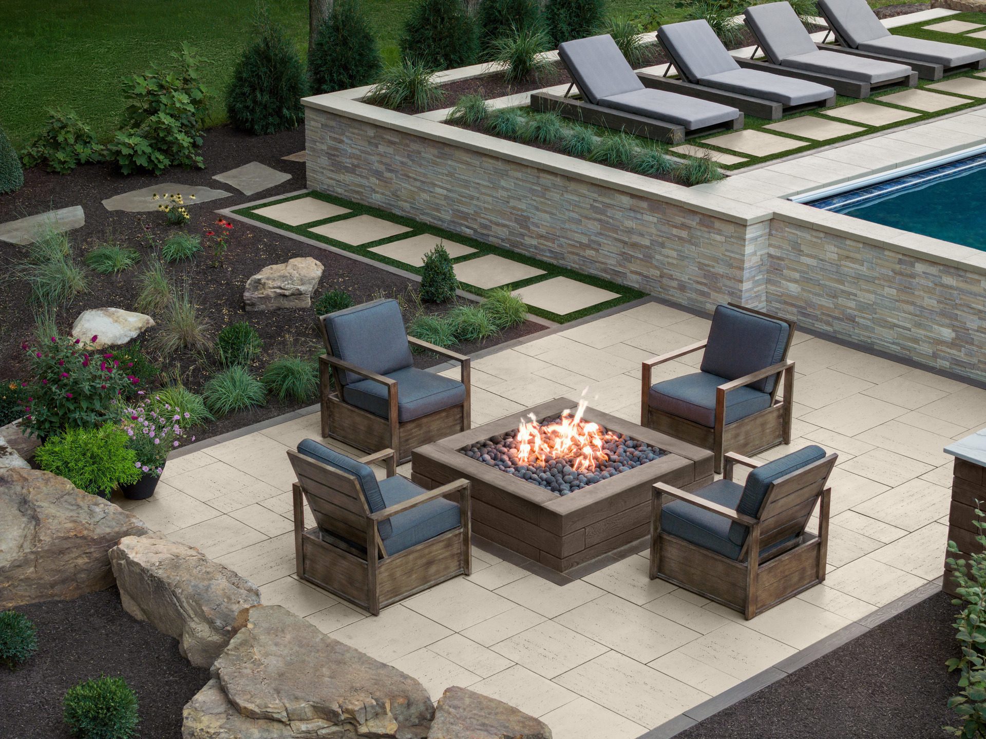 Seating area around a firepit beside garden beds and a pool in a residential backyard. 